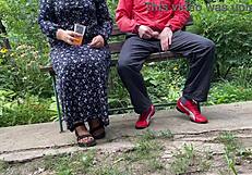 Milf subtly jerks big dick into glass on park bench